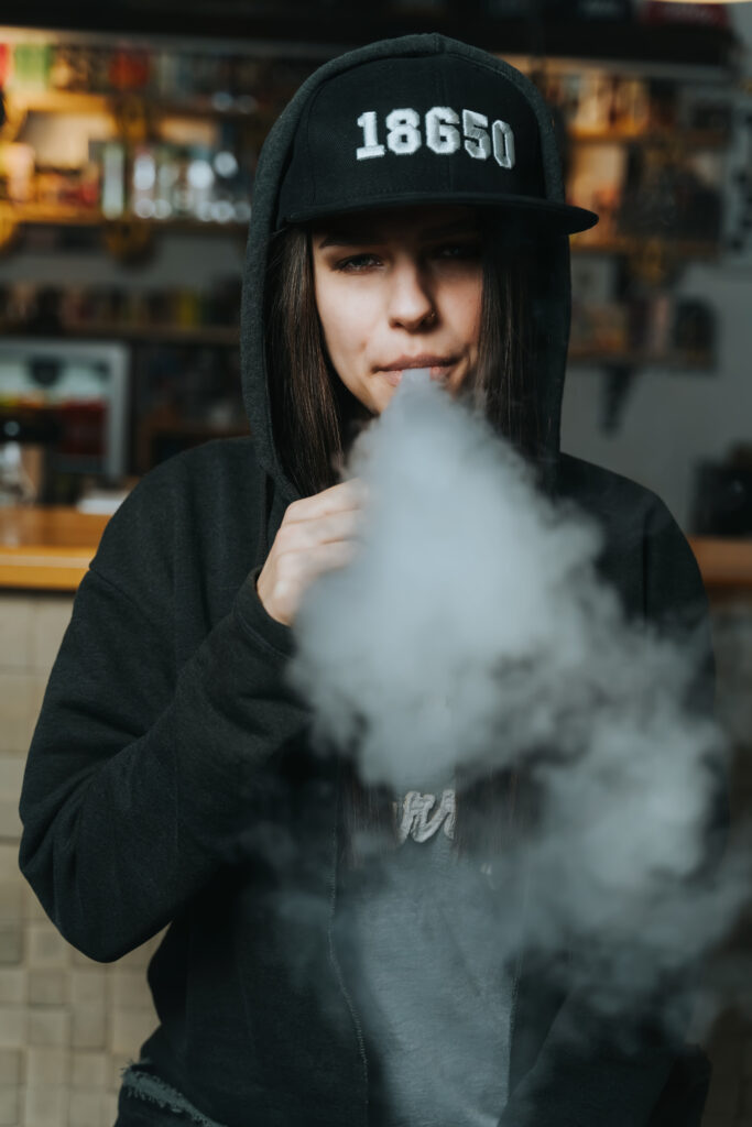 Woman in cap smoking an electronic cigarette at the vape shop