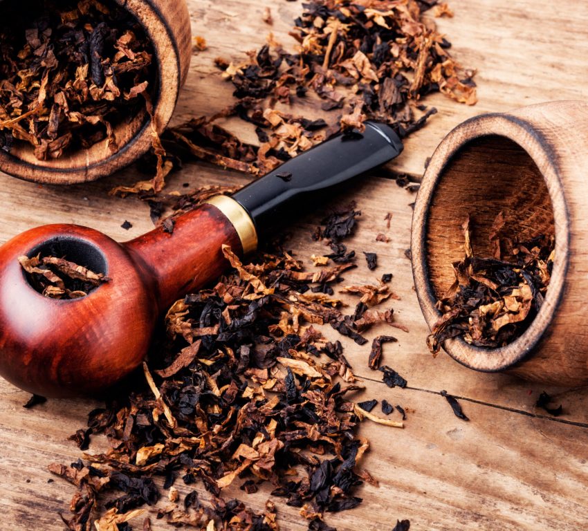 A close-up photo of loose tobacco next to a wooden tobacco pipe.